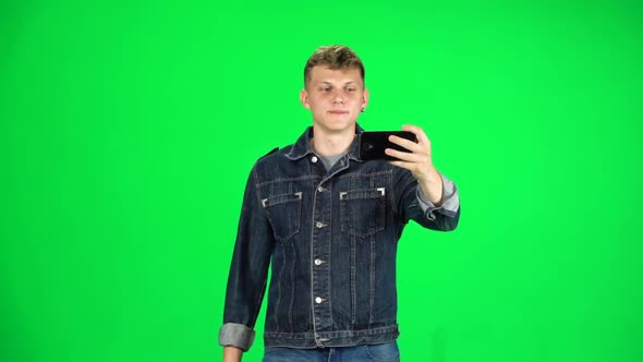 Smiling Guy Goes and Takes a Selfie with Smartphone on Green Screen at Studio. Slow Motion