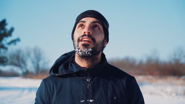 Portrait of a Happy Man with a Beard in a Winter Hat Covered in Snow Smiling