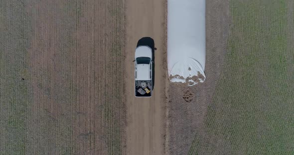 Aerial view of 4x4 pickup truck driving through wheat crops field with silos bags on the road. Argen