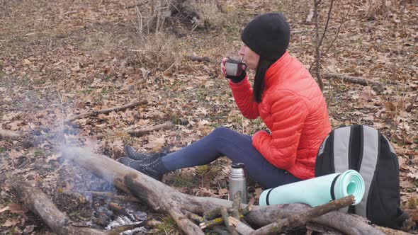 Girl Having Rest with Hot Drink, Tea From Thermos Sitting on the Tree in the Forest.