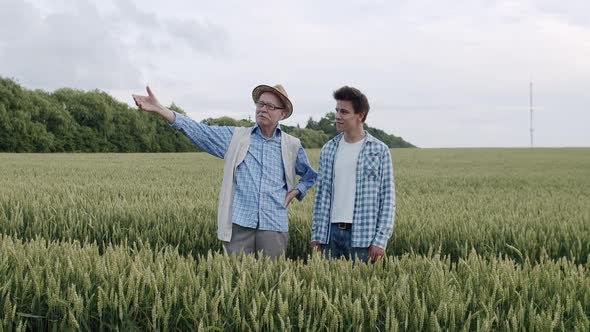 Two Happy Farmers Having Talk and Crossing Hands in Green Wheat Field