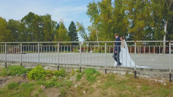 Newly Wedded Couple Walks Along Fence in Green Park