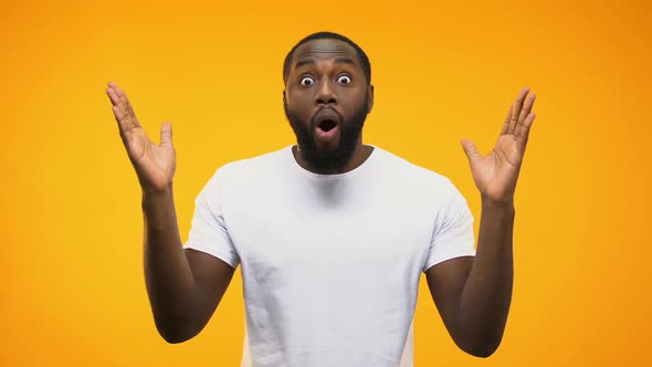 African American Man Is Amazed, Throwing Up Arms, Isolated on Yellow Background
