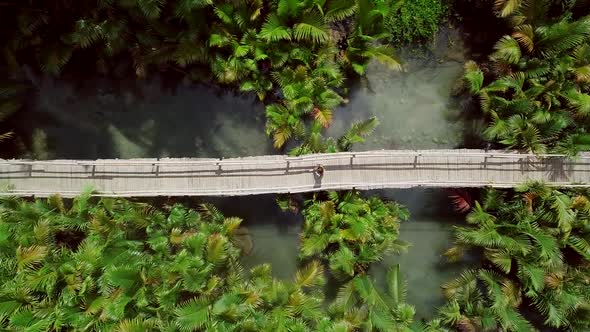 Aerial view of woman walking on long wooden bridge in Bojo river, Philippines.