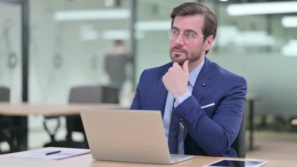 Pensive Young Businessman Thinking and Working on Laptop 