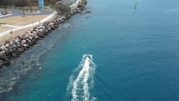 Drone following a person on a electric surfboard travelling along a ocean waterway