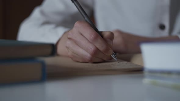 Closeup of female hand making notes, writing letter in personal diary with books.  Library Education