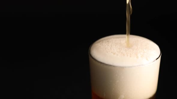 Close up pouring beer with bubbles and foam in glass on black background