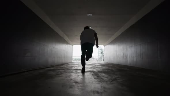 Silhouette Man Runs Along an Underground Passage Into Light From the Darkness