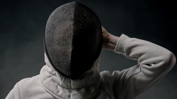 Fencing Training in the Dark Studio - Young Woman Putting on a Helmet and Stands in the Position