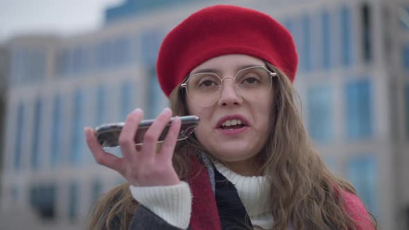 Headshot Portrait of Joyful Young Caucasian Millennial in Beret and Eyeglasses Recording Voice