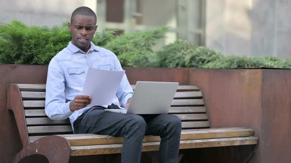 African Man Having Loss Working on Papers and Laptop