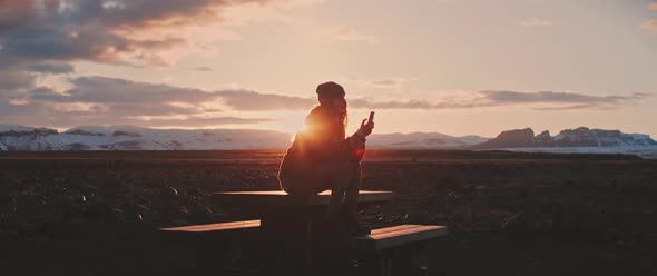 Person sits during sunset while on phone