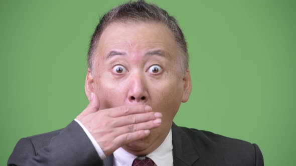Mature Japanese Businessman Surprised Against Green Background