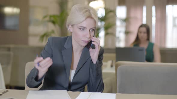 Busy Confident Businesswoman Talking on the Phone in Restaurant and Writing Notes. Portrait of