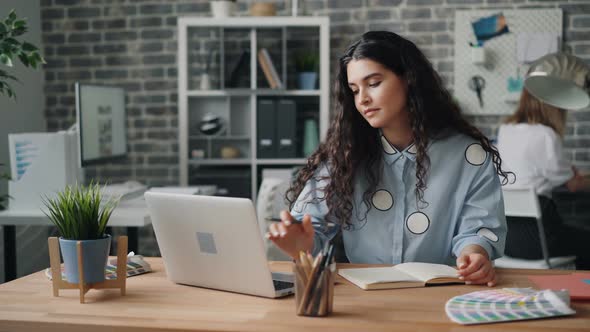 Young Lady Writing in Notebook and Working with Laptop in Office