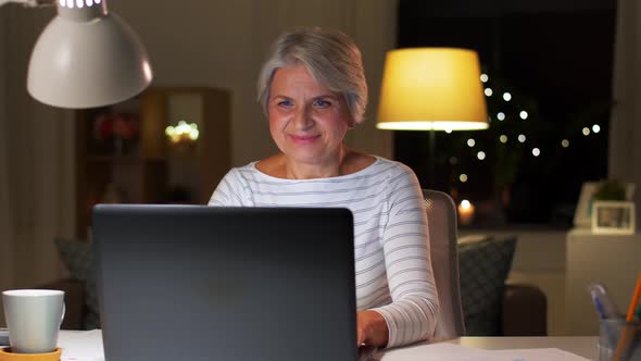 Happy Senior Woman with Laptop at Home in Evening