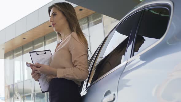 Female Insurance Broker Holding Contract and Waiting for Client Near Automobile