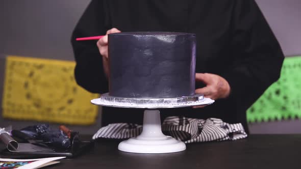 Step by step. Baker applying glittery dust with brush to a black multilayer cake.