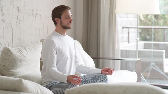 Mindfulness Young Man Sits on a Sofa in the Living Room and Meditates a Calm Mood Relaxing in a