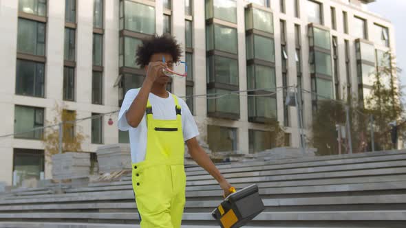 Portrait of Confident Afro Technician in Uniform Overall and Plastic Glasses Holding Toolbox Outdoor