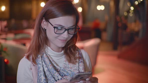 Attractive Girl with Glasses Holding Mobile Phone Is Chatting with Friends on Social Network