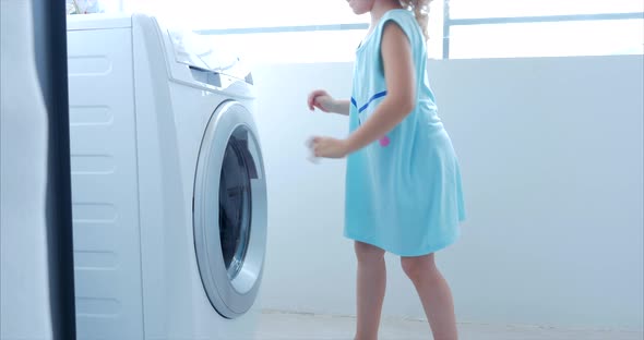 Little Girl Loads the Laundry in the Washing Machine and Includes Washing