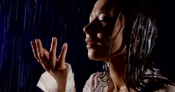 Young Brunette Is Getting Wet Under Rain in Night Outdoors, Holding Palm Up and Looking To Heaven