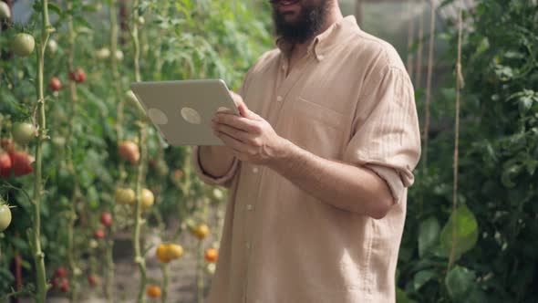 Smiling Unrecognizable Male Gardener Standing in Greenhouse Using Tablet