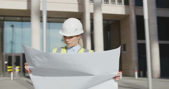 Architect in Protective Helmet Holding Blueprint in Front of Office Building