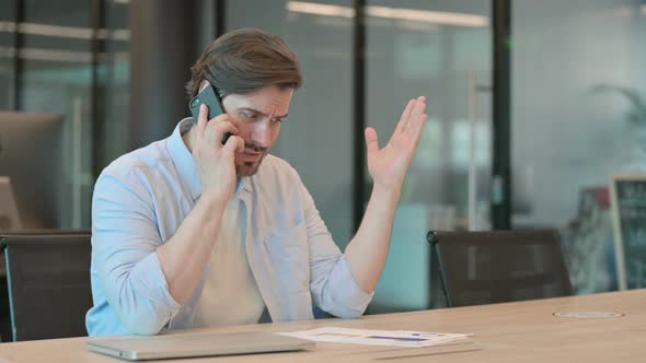 Angry Mature Adult Man Talking on Phone in Office