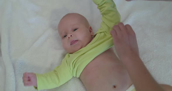 Mother Putting Diapers on Cute, Baby on Bed, Who Looking at Camera