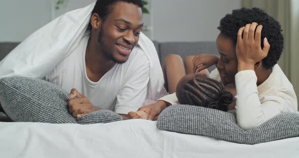 African Family Lying on Sofa on Gray Pillows Covered with White Warm Blanket Afro Mother and Ethnic