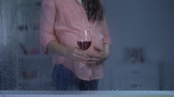 Pregnant Woman Stroking Tummy and Drinking Wine on Rainy Day