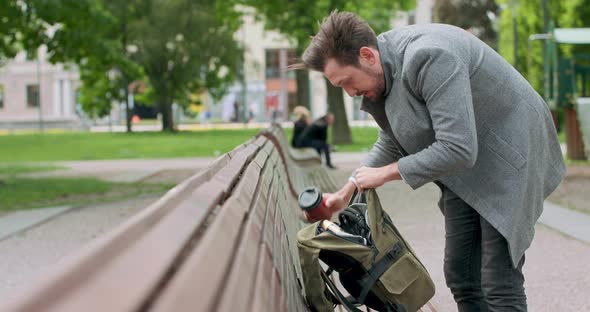 Young Man with Mustaches and a Beard is Searching for Something in His Backpack Placed on the Wooden