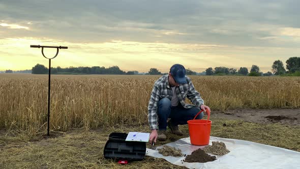 Agronomist Pouring Soil Sample From Bucket Taking Notes at Field Dawn
