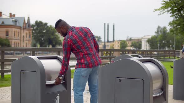 Young African Guy Throwing Empty Water Bottle in Trash Can on City Street