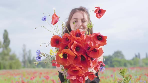 Pretty Young Girl in a Poppy Field Holding Bouquet of Flowers in Hands Looking in the Camera