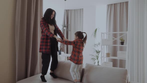 Full Length Positive Mother and Little Daughter Having Fun Jumping Together on Sofa in Living Room