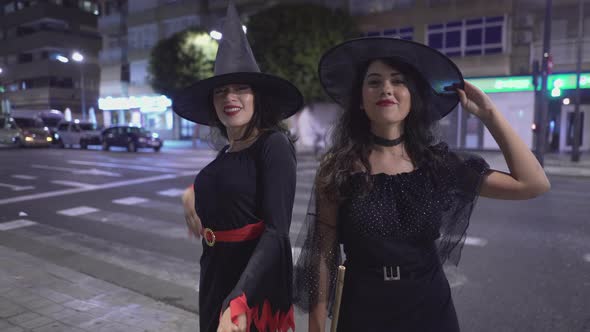 Young Women In Black Witch Costumes Doing Hand Movements While Posing At The Camera In The Street