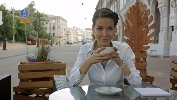 Woman Drinking a Coffee From a Cup in a Restaurant Terrace While Thinking and Looking Sideways