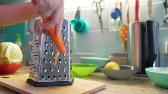 Woman Grinds Orange Carrots on Silver Metal Grater in the Kitchen on Blue Board for Cooking