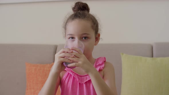 Cute Little Girl Drinking a Glass of Milk in the Kitchen at Home