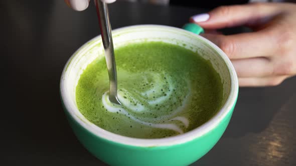 Woman Takes Green Foam Off Matcha Latte with Teaspoon