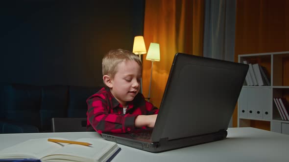 Cute Preschooler Boy is Sitting at Home in the Evening Typing on Laptop and Thinking About a alt