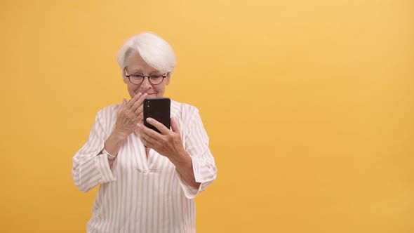 Emotional Senior Woman Receiving Good News on the Smartphone. Putting Hand Over Her Mouth