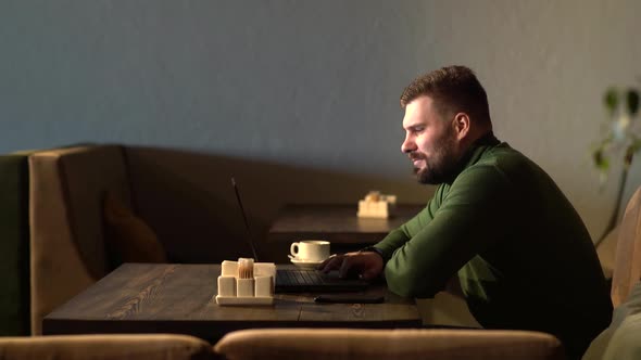 the Man Is Satisfied with the Work Done. Happy Young Man Working on a Laptop While Sitting in a Cafe