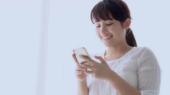 Beautiful young asian woman smiling standing looking smart phone reading social network.