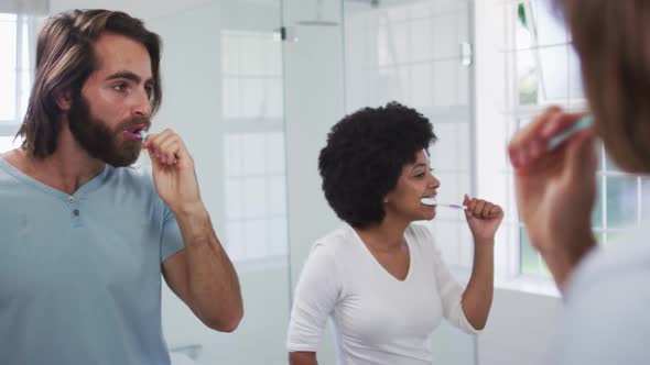 Mixed race couple brushing together while looking in the mirror at bathroom