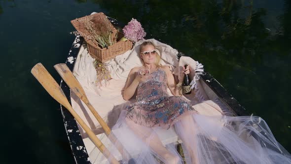 Rich girl enjoying a glass of expensive champagne in rowboat floating in lake